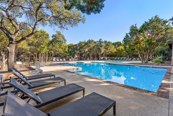 A pool surrounded by trees and sun loungers.